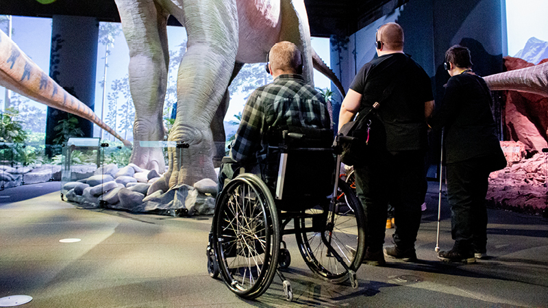 Kuvassa kolme Elä täysii -klubilaista Tiedekeskus Heurekassa katsomassa dinosaurus -näyttelyä klubin esteettömällä retkellä.